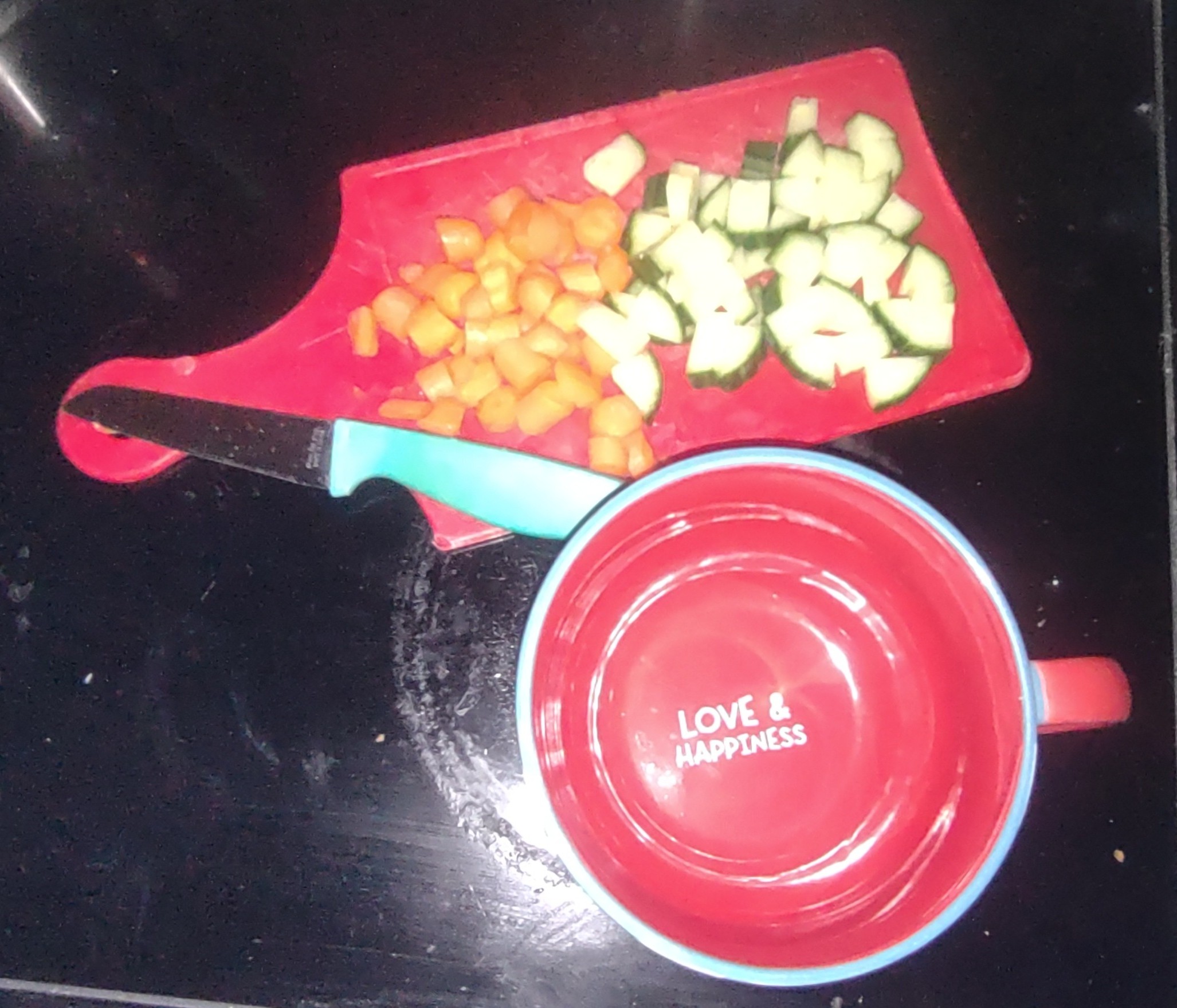 picture of diced carrots and cucumbers on a red cutting board next to a large mug that says LOVE AND HAPPINESS on the inside